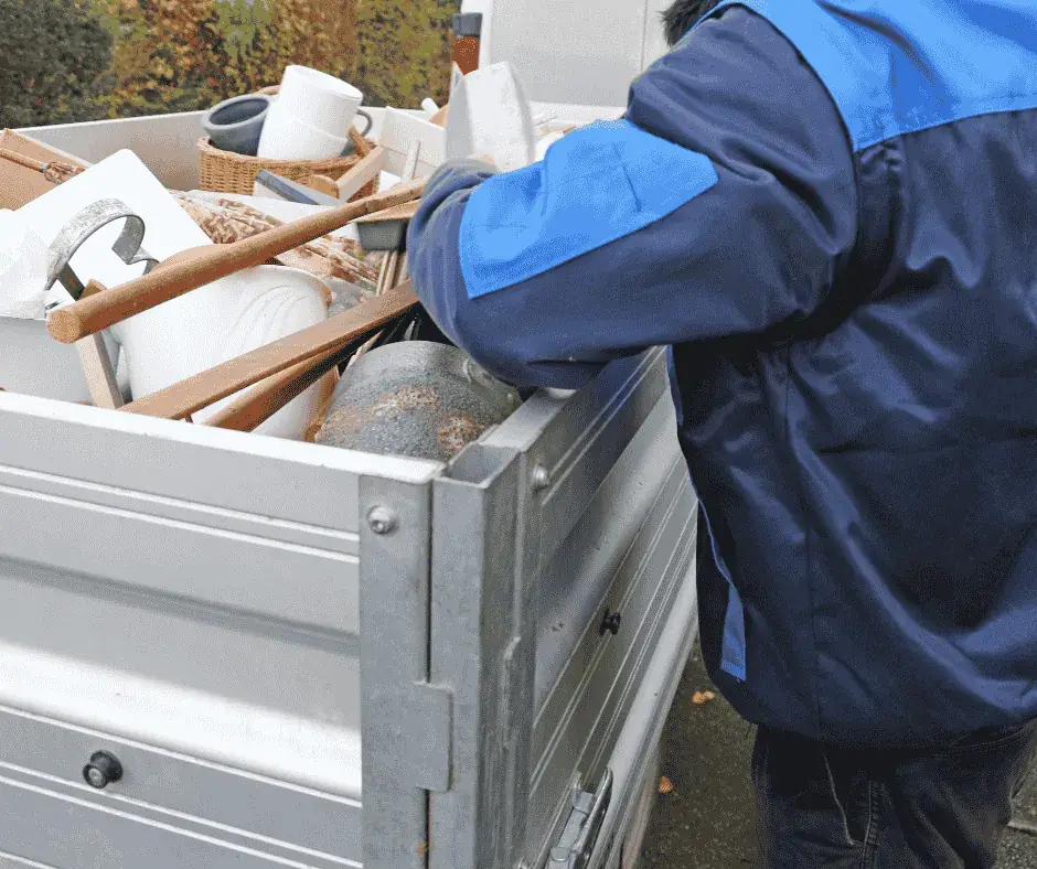 Entrümpelung von Keller und Garage: Helfer in Arbeitsjacke lädt ausgeräumte Gegenstände zum Abtransport auf einen Anhänger